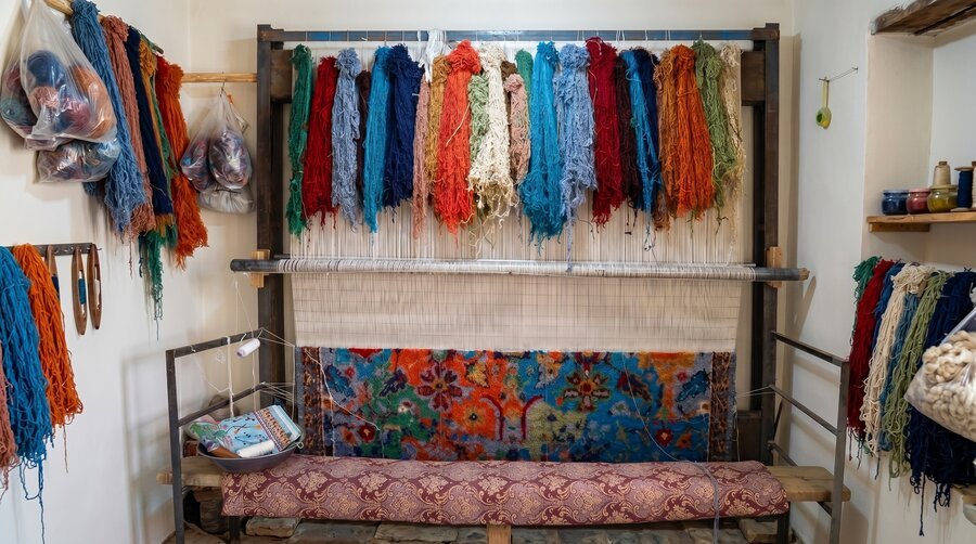 A carpet loom mid-work, with knotted sections at the bottom and unwoven threads above