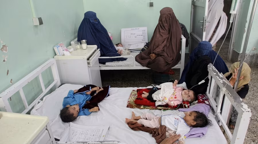 Three children sharing a hospital bed in a crowded pediatric ward at Sehat-e-Tifl children's hospital in Kabul