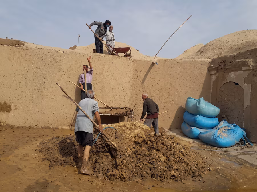 Workers mixing straw into wet clay for kah-gil on a rooftop, with sacks of straw stacked beside them