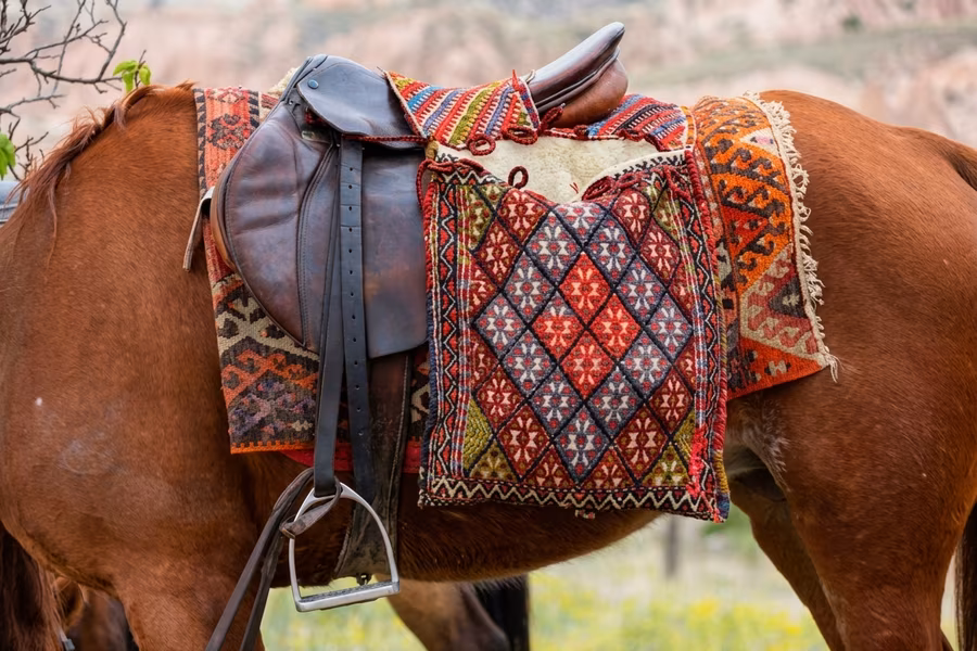 A khurjin draped over a horse&rsquo;s back beneath a leather saddle, geometric patterns along both hanging sides