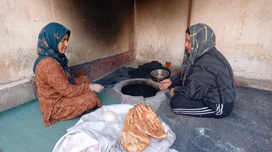 Two women kneading dough beside a home tandoor
