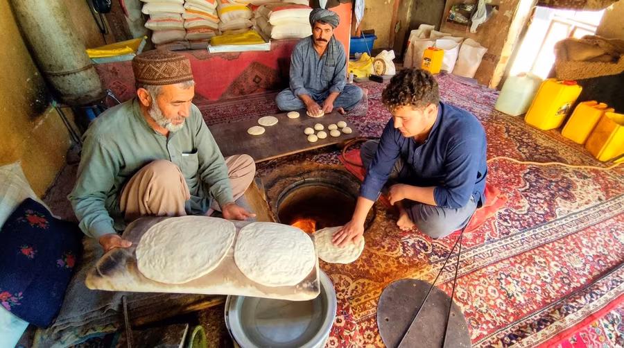 Men baking bread the traditional way, gathered around a tandoor sunk into the floor