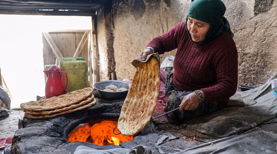 A woman pulling a finished round of tandoor bread off the oven wall with a cloth