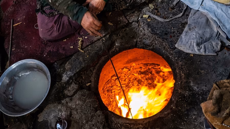 A hand tending the glowing wood fire inside a clay tandoor oven