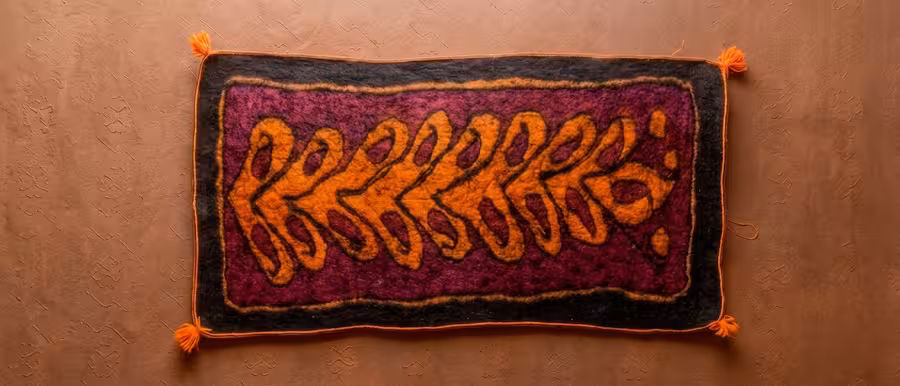 A finished Afghan namad with an orange botanical pattern, lying flat on a floor